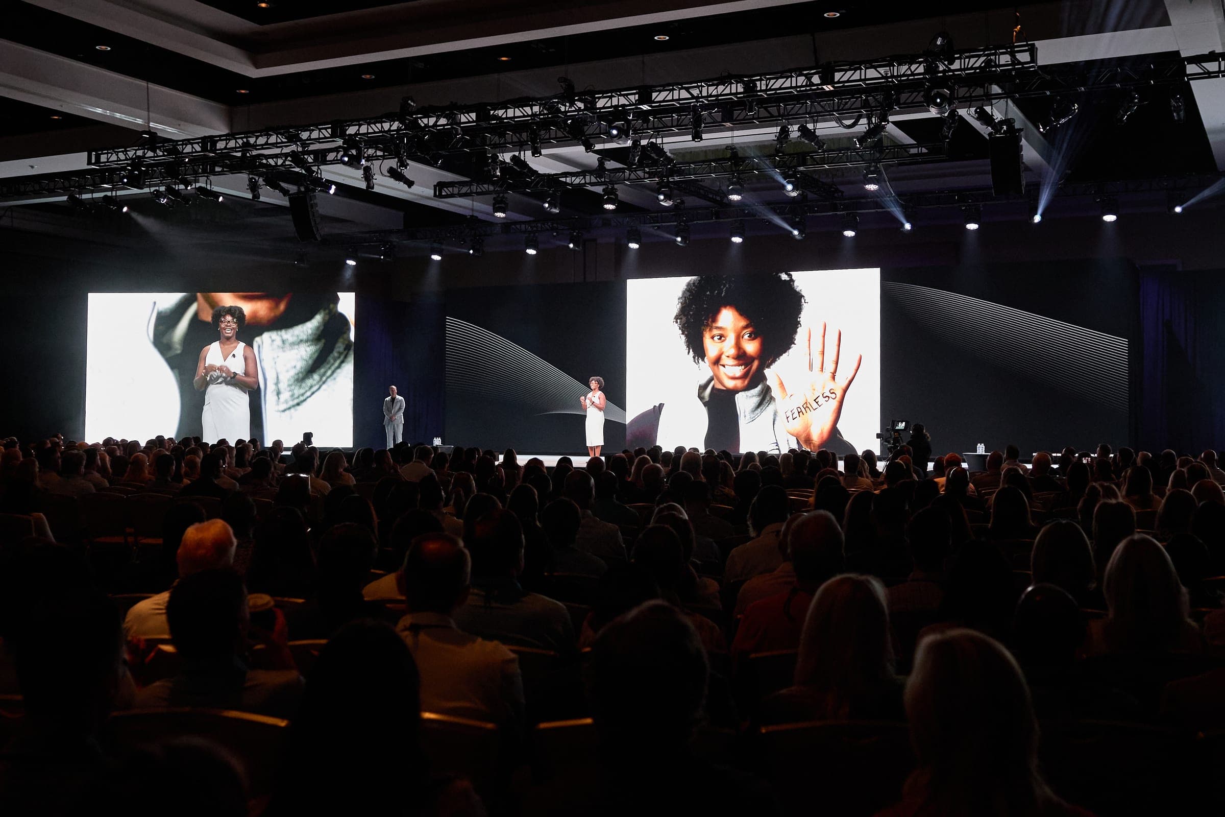 A wide view of the Brain Tattoo closing reveal, two large screens showing participant portraits above a full ballroom audience.